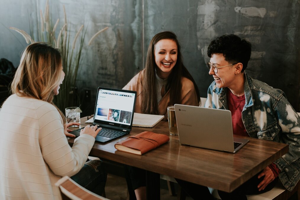 Image curtesy of Brooke Cagle, Unsplash A group of digital nomads laughing at a table with their laptops