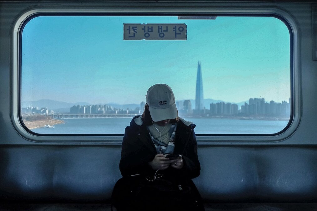 Photo by Elle Morre on Unsplash Woman sitting on Korean train with a city in the background.