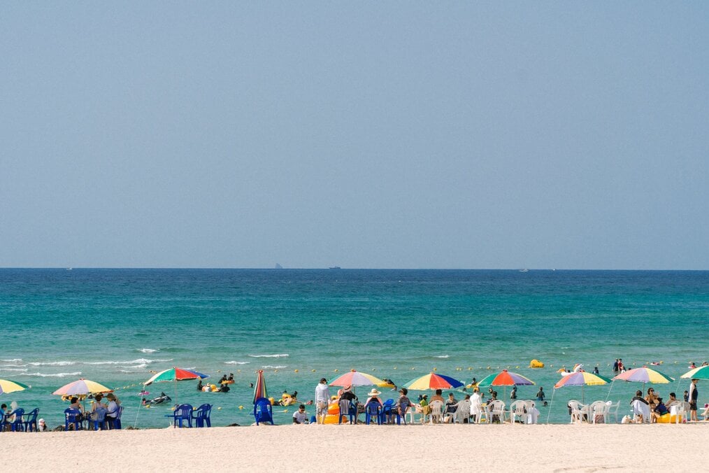 Photo by jaemin don on Unsplash People on a white sand beach with clear blue water.