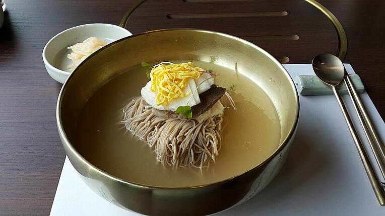 Grey noodles in broth in a metal bowl, topped with a hardboiled egg.