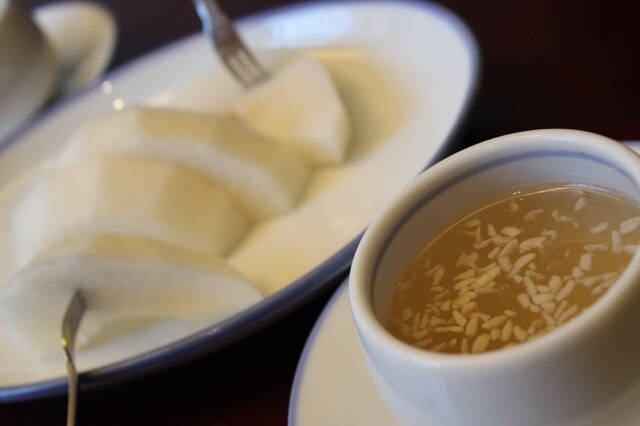 A cup of Korean rice drink sikhye with a plate of coconut in the background.