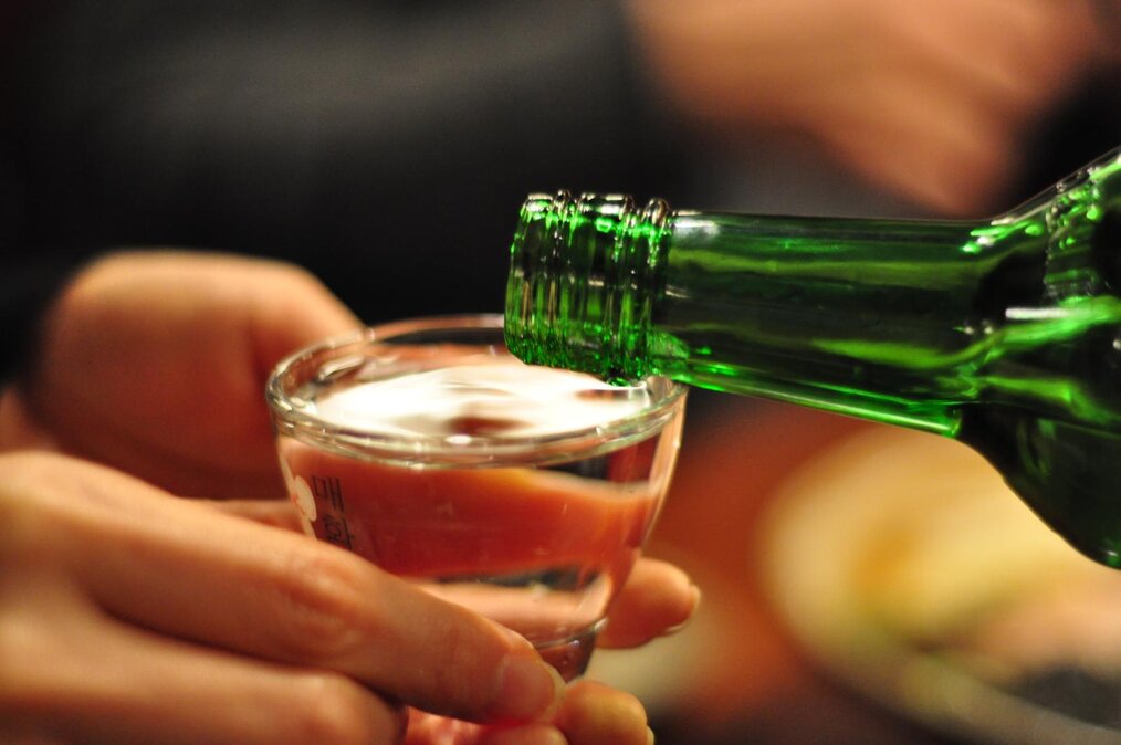 Graham Hills, CC BY 2.0 via Wikimedia Commons A hand holding a small glass of clear liquid.