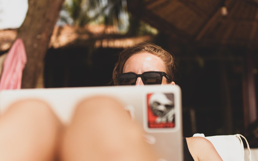 Image curtesy of Anton Shuvalov, Unsplash A digital nomad sitting in the sun on her laptop with her glasses on