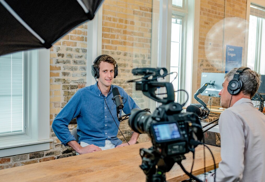 Image curtesy of Austin Distel, Unsplash A guy in a blue button down shirt hosting a podcast