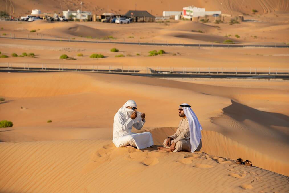 Two men wearing Kanduras sitting on a sand hill in the desert