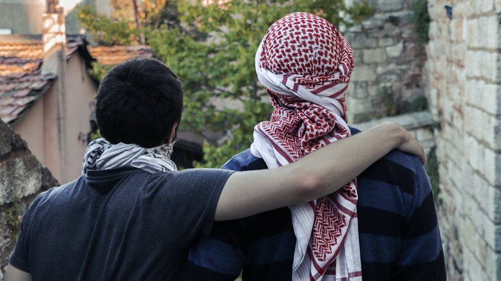 Image curtesy of Sohaib al Kharsa, Unsplash A student putting an arm around the shoulders of an older gentleman wearing a headscarf