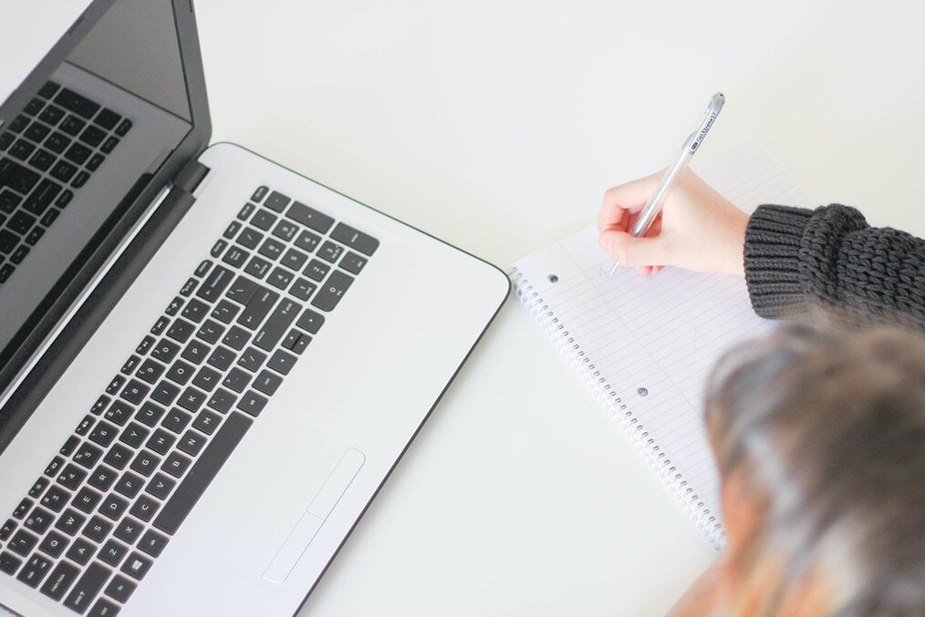 A person making a checklist while sitting at a laptop