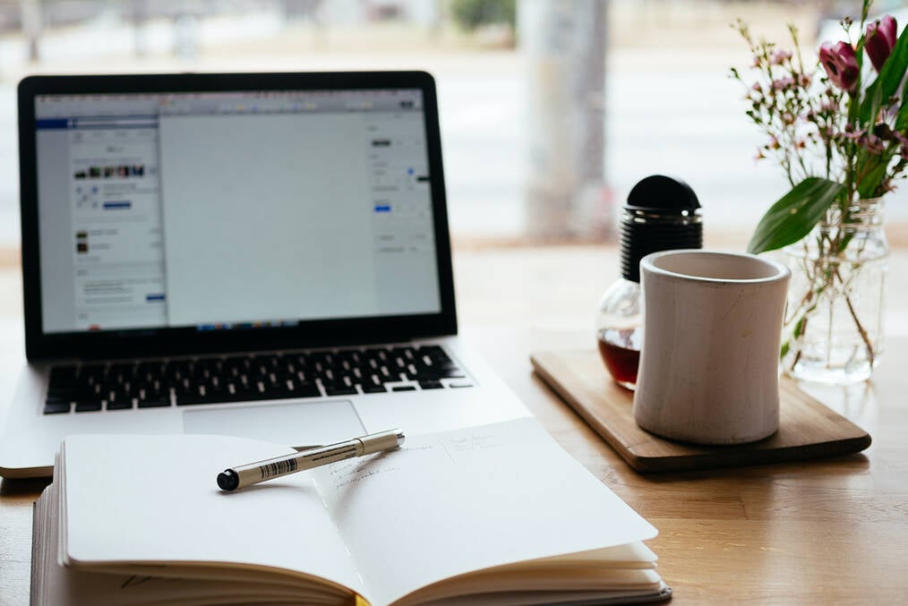A notepad, computer, and glass of tea sitting at a desk