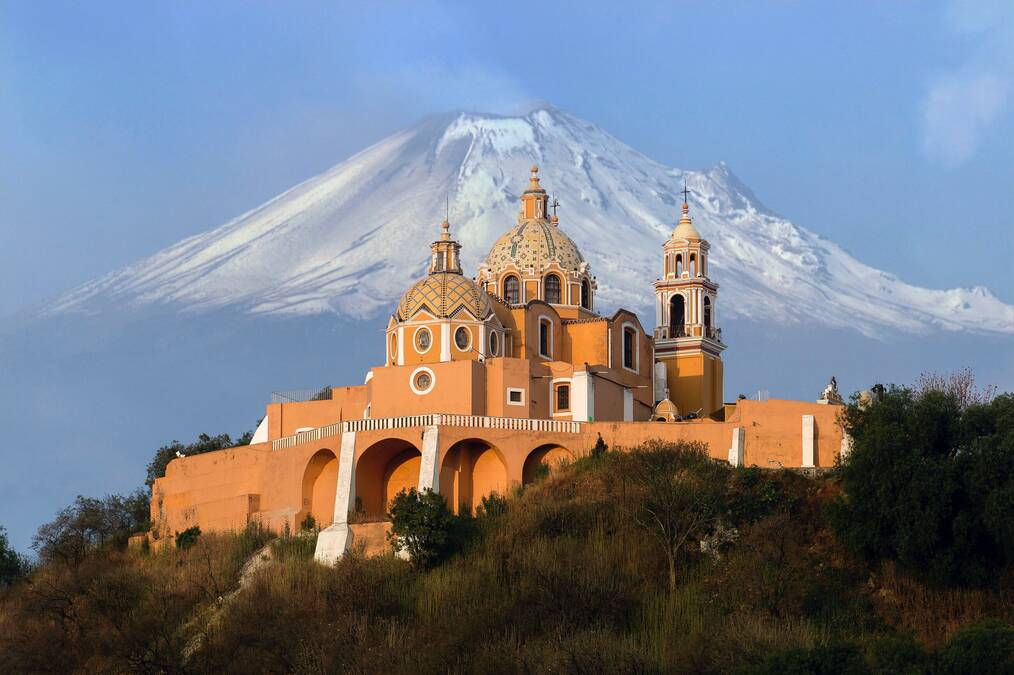 An elaborate building in Mexico with a large snow-covered mountain in the background.
