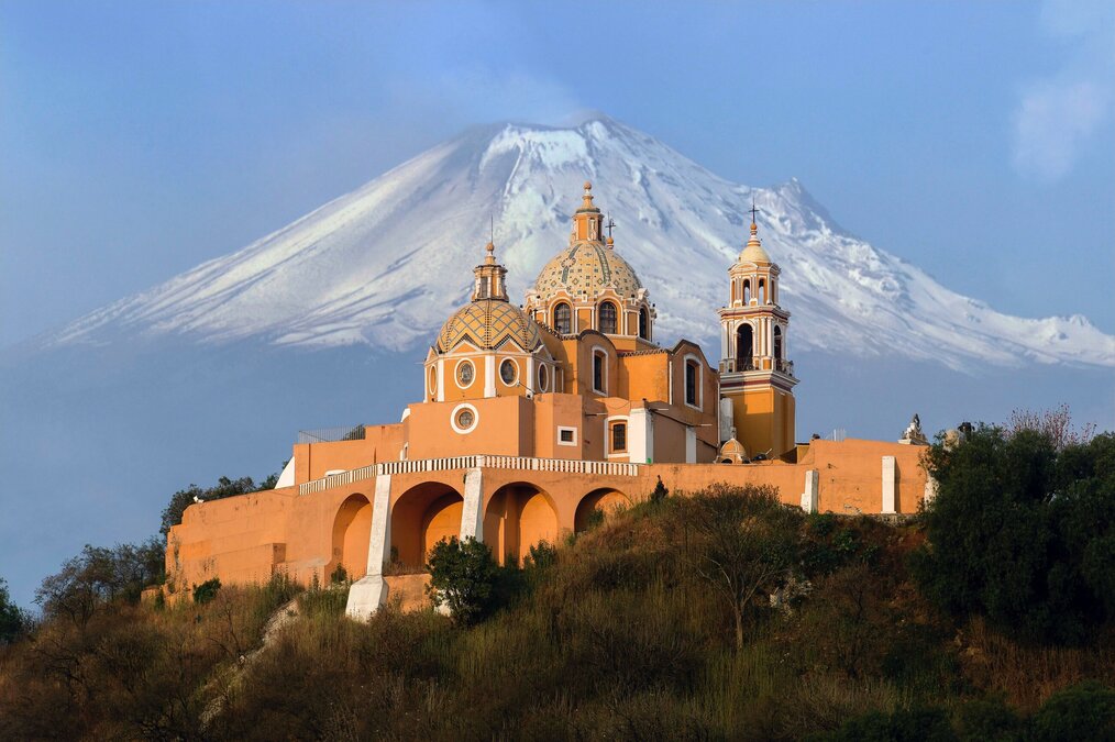 Photo by Pedro Lastra on Unsplash An elaborate building in Mexico with a large snow-covered mountain in the background.