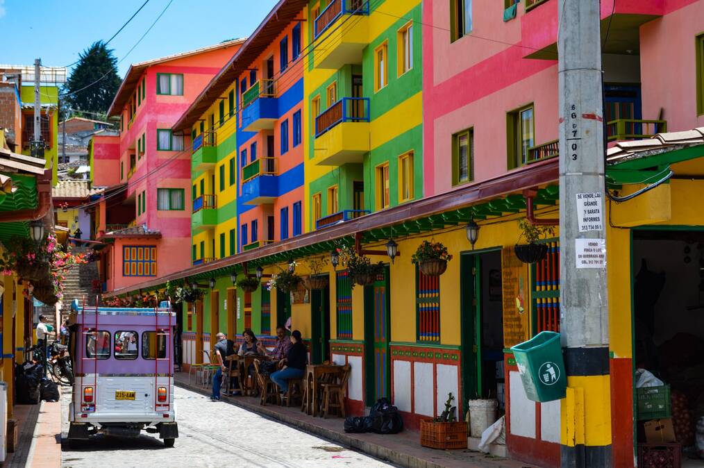 A bus sits on a street with colorful buildings in Colombia.