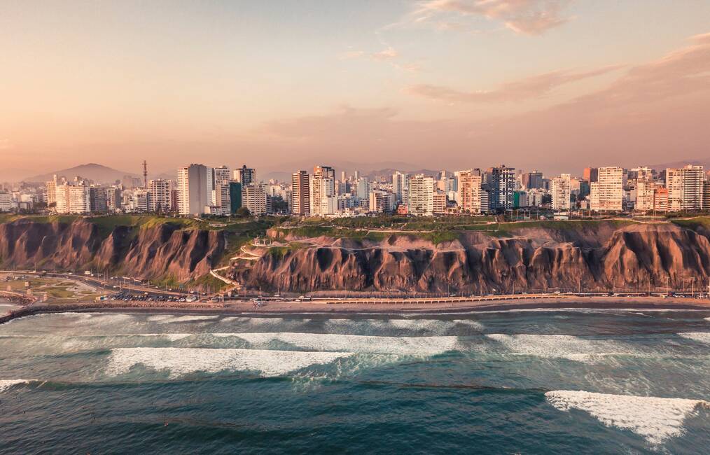 Waves crash along the cliffs with city buildings above.