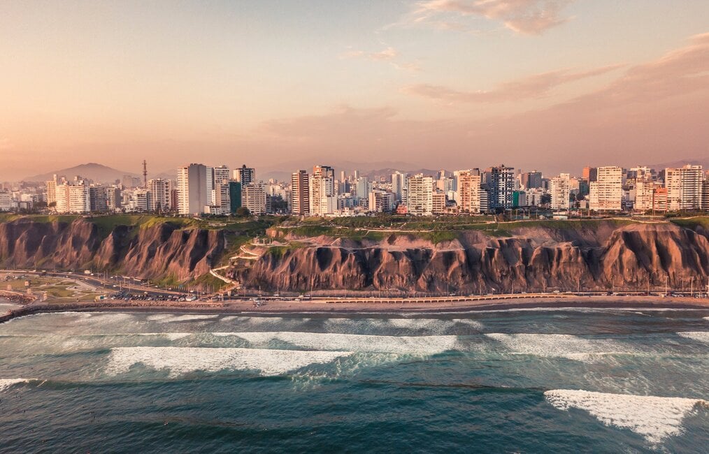 Photo by Willian Justen de Vasconcellos on Unsplash Waves crash along the cliffs with city buildings above.