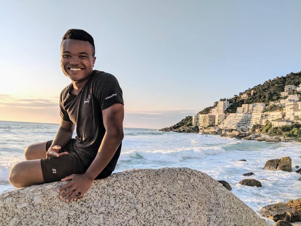 Alfred sitting on a boulder at the beach in South Africa smiling