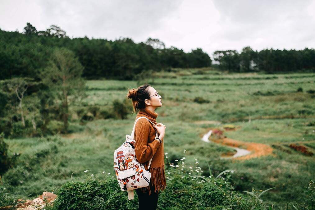A woman standing alone in a field with a backpack.