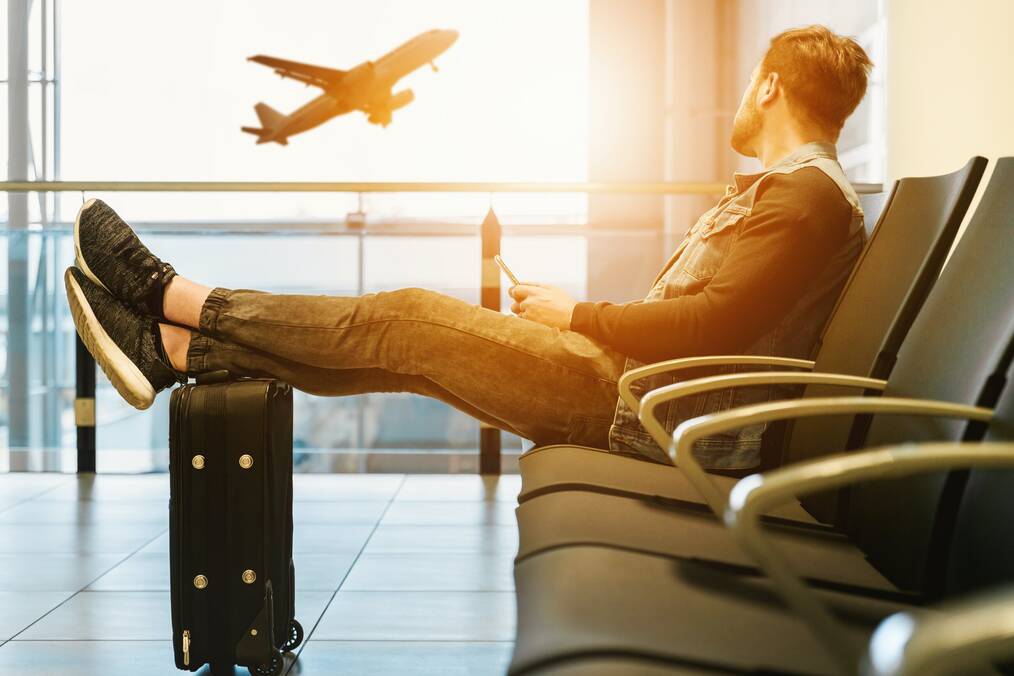 Man sitting with his feet up on a suitcase while a plane takes off in the background.