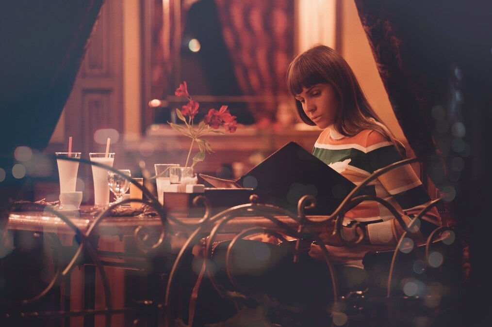 Photo by Oleksandr Pidvalnyi A woman sitting alone at a restaurant looking at a menu.