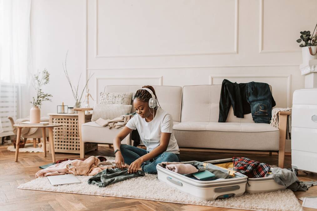 A woman sitting on the floor packing a suitcase.