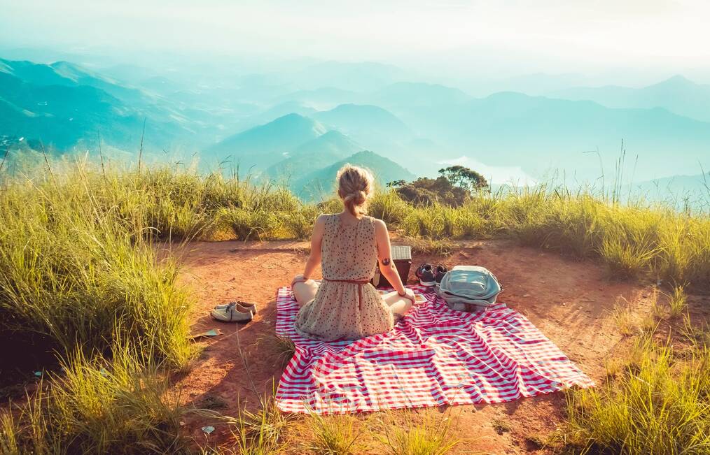 A woman sitting on a blanket alone facing the mountains.