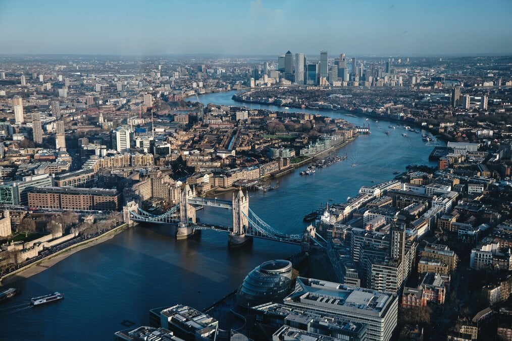 Photo by Frans Ruiter on Unsplash An aerial view of the city of London with buildings and a river.