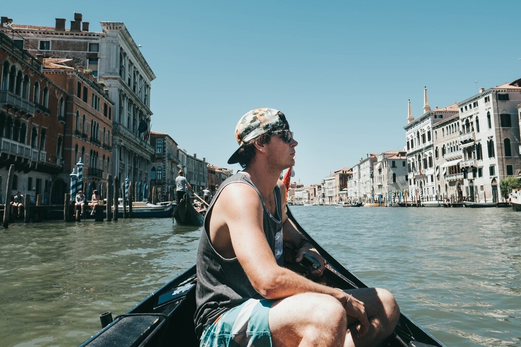 Image curtesy of Hank Paul, Unsplash A person wearing a muscle tank and backwards cap on a gondola in Venice