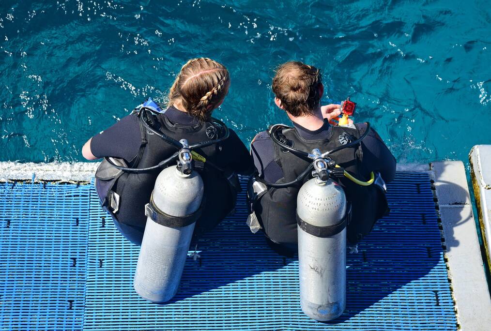 Two divers sitting on a boat with oxygen tanks.