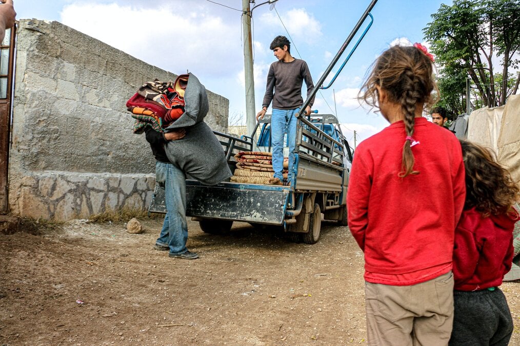 Photo by Ahmed akacha Two little girls watch a man unload blankets from a truck.