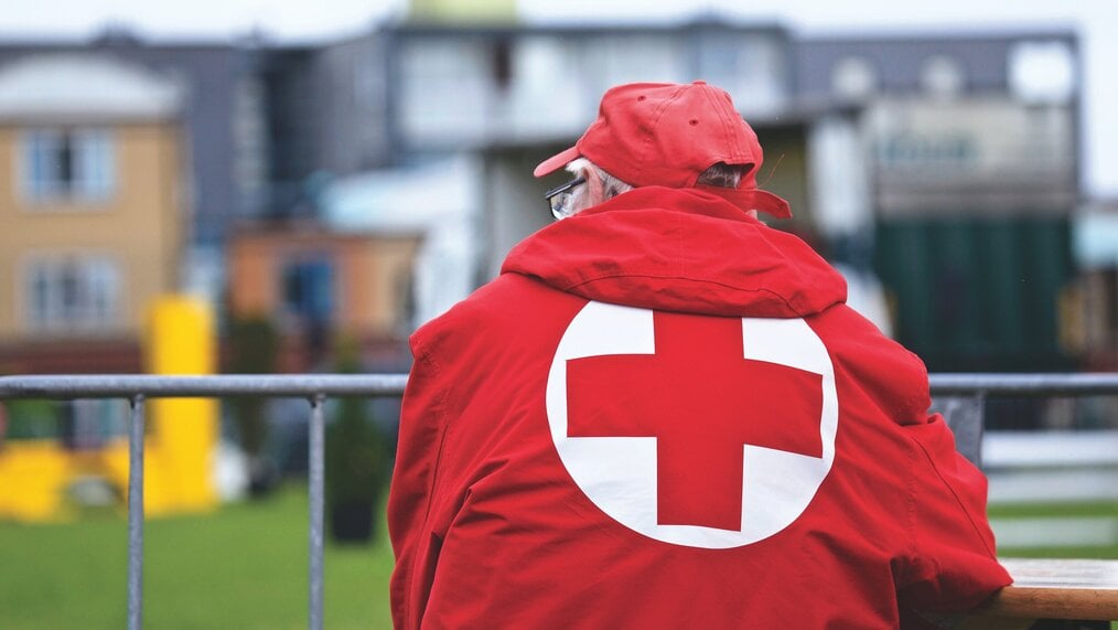 Photo by Matthias Zomer An older white man with his back to the camera wearing a red cross coat.