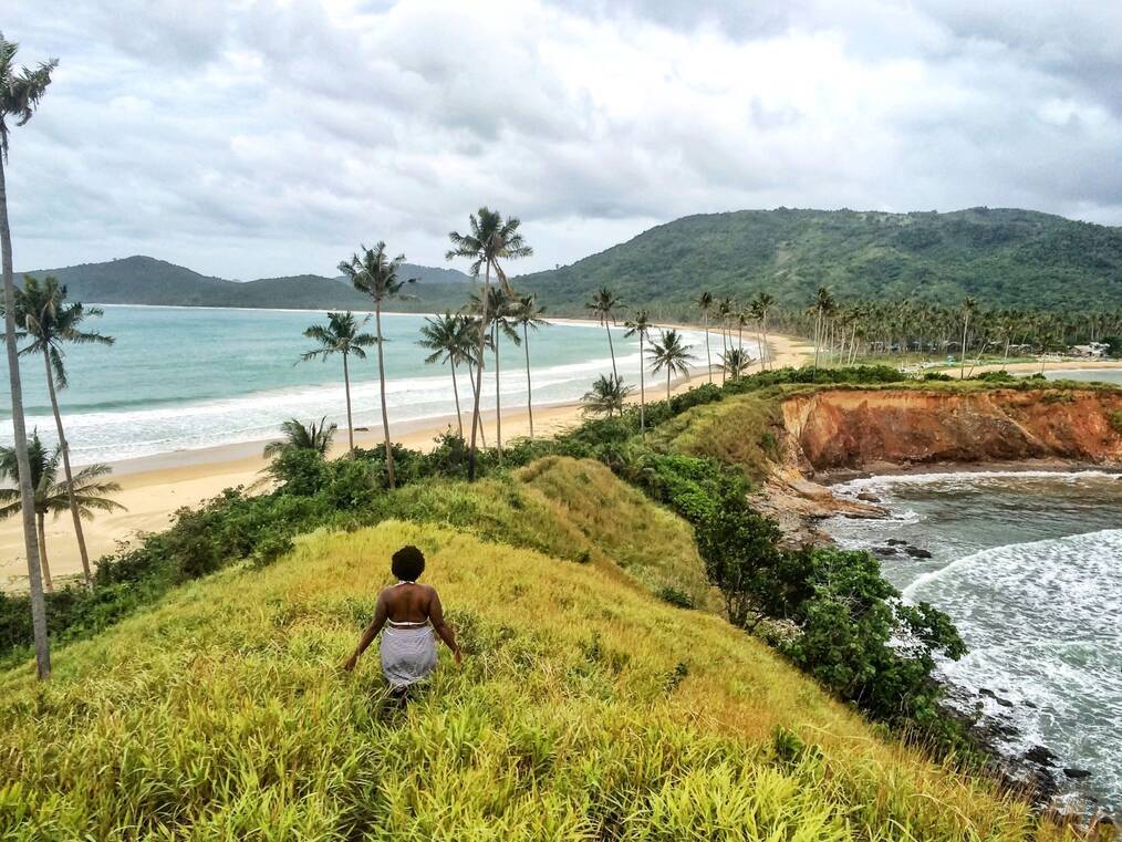 A woman stands with her back to the camera on the shore.