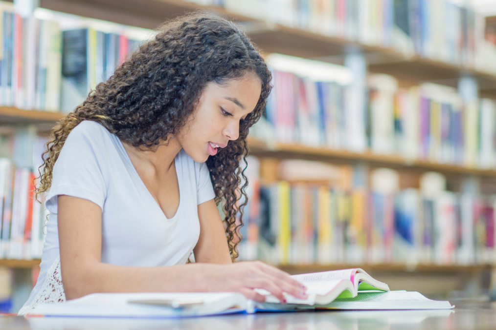 A person with a blue shirt and brown curly hair reading a book