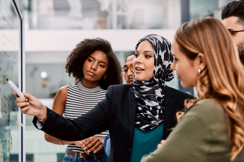 A person wearing a hijab demonstrating to her coworkers on a white board