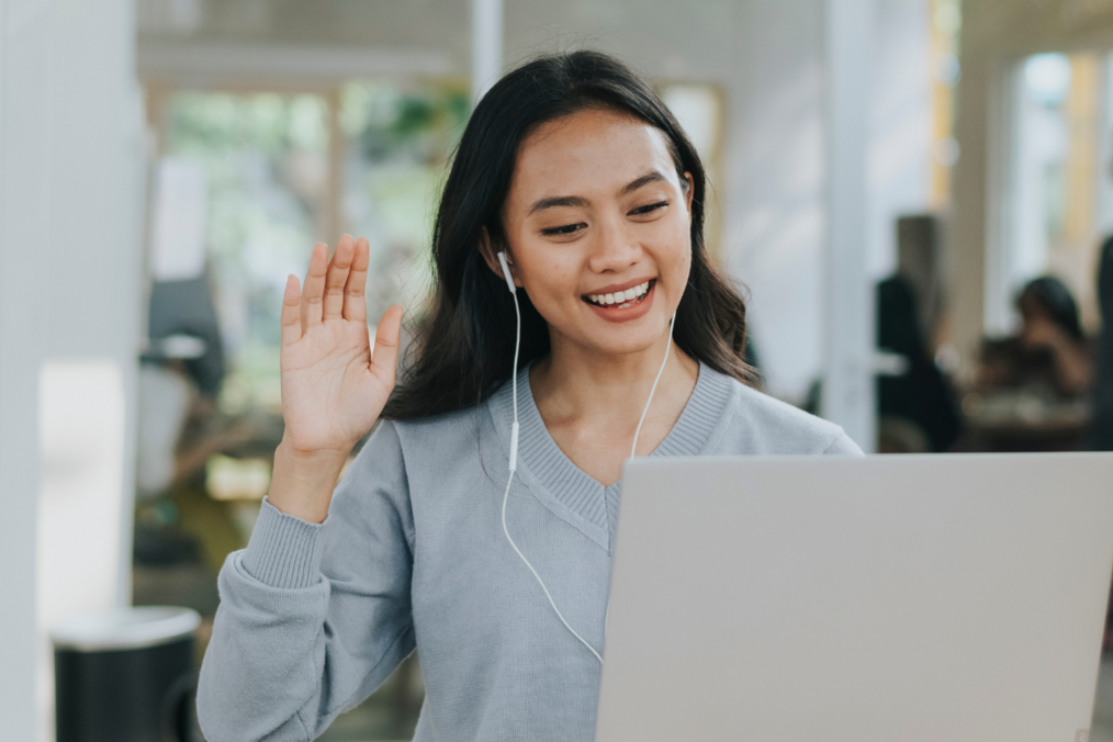 I person with brunette hair and headphones on waving at a computer screen