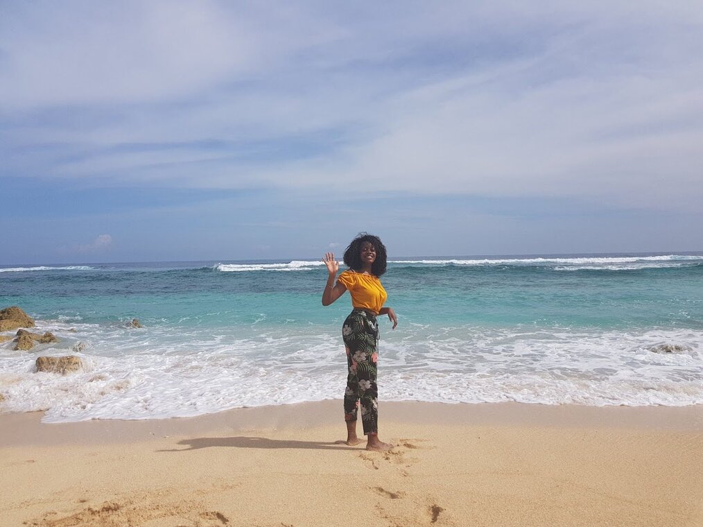 Sanyu, IVHQ Bali A person in a yellow top and colorful pants waving and smiling on the beach in Bali