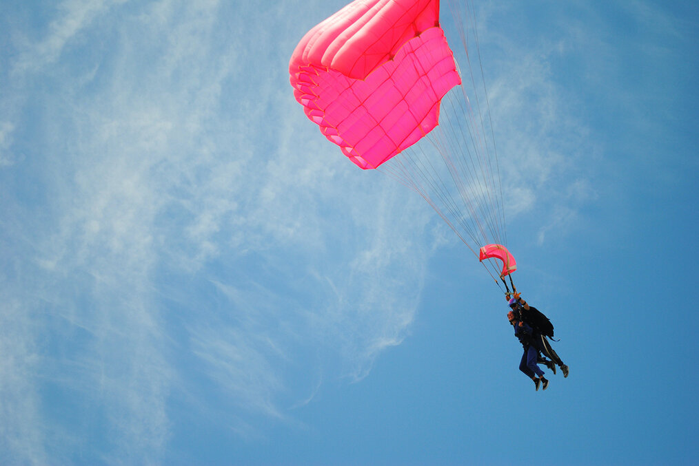 A skydiver with a red parachute gliding to the ground in New Zealand