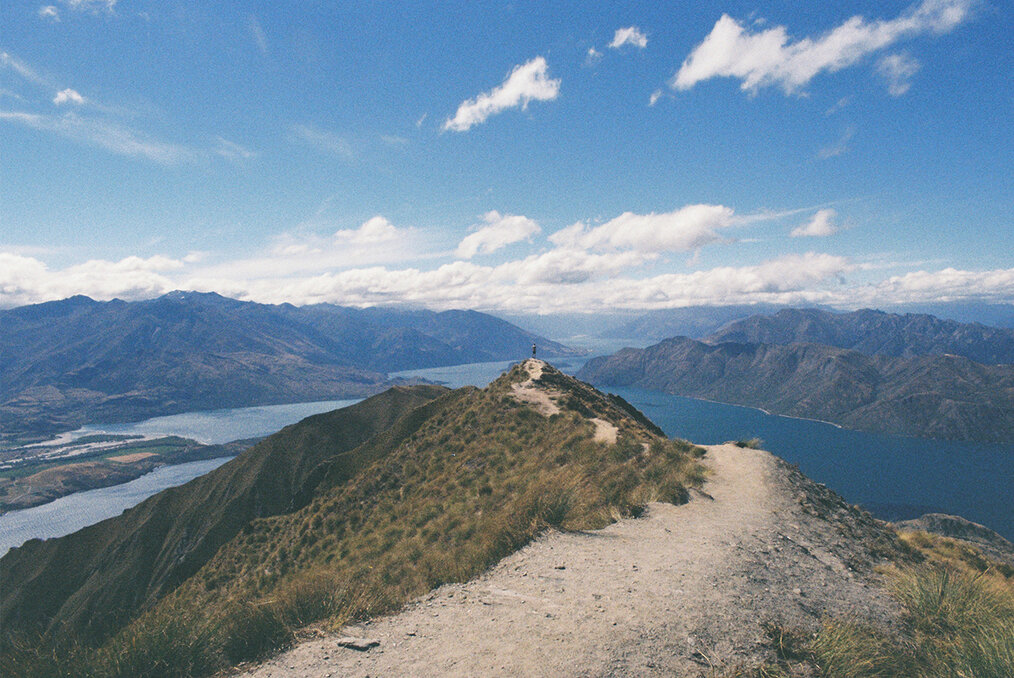 A sweeping view of a hiker at the summit of Roys peak in Wanaka, New Zealand