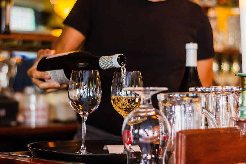 A server pouring a glass of white wine at a dinner table in a restaurant