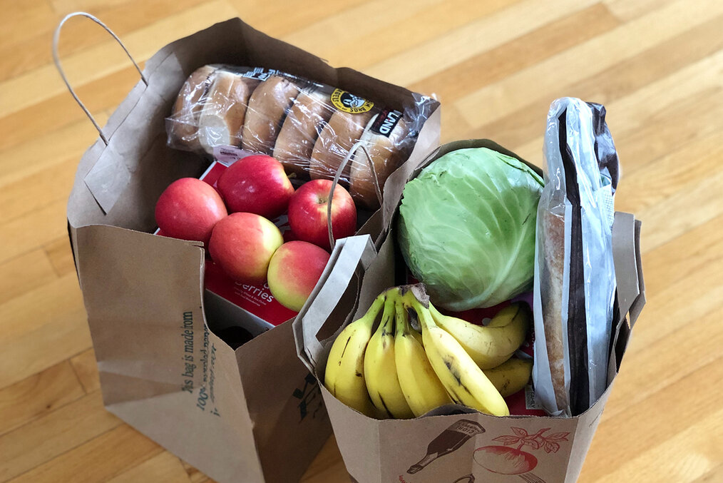 A couple bags of groceries, including bananas, apples, and bagels