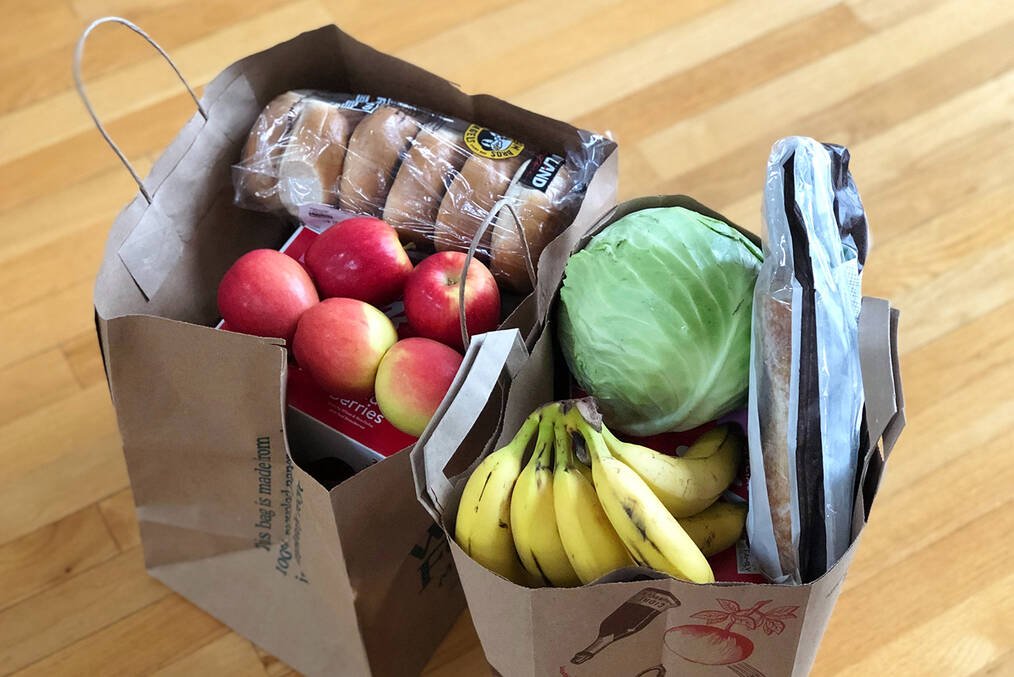 A couple bags of groceries, including bananas, apples, and bagels