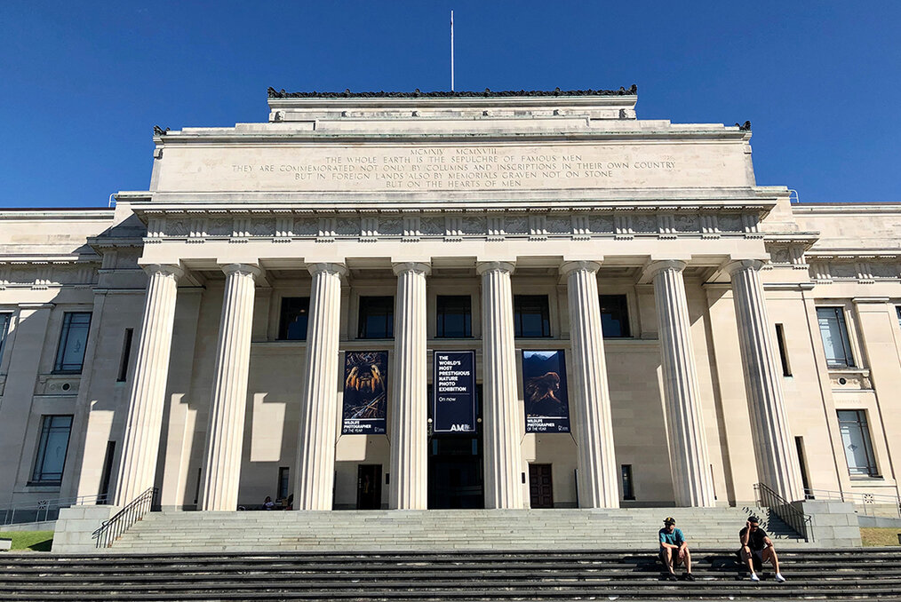 Two people sitting on the steps in front of the war memorial museum in Auckland, New Zealand