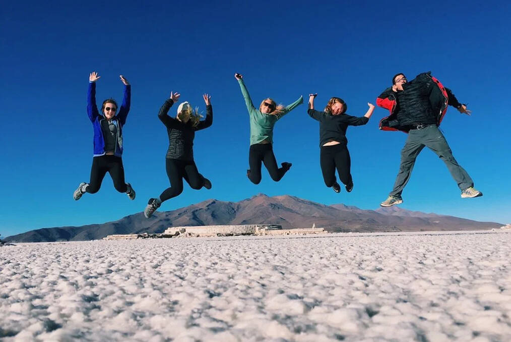 A group of five people jumping on a beach