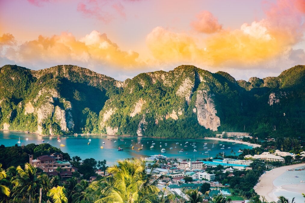Image curtesy of Evan Krause, Unsplash A yellow, pink, and orange sunset over a bay with high mountains in Thailand