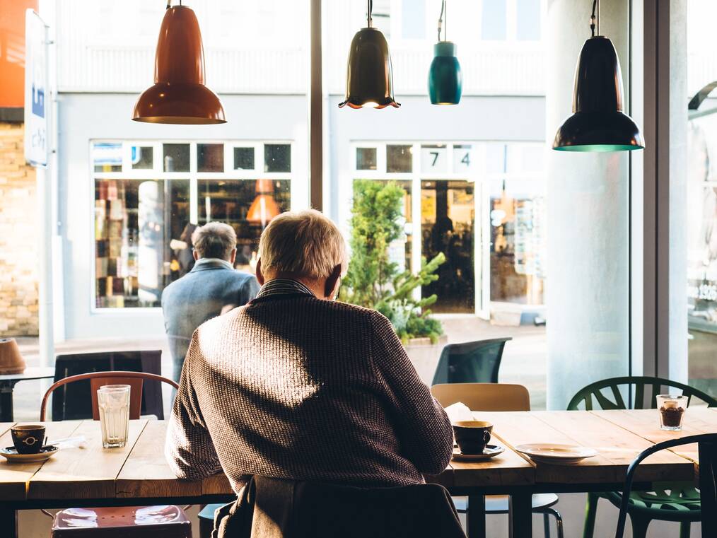 An older adult sitting at a cafe staring out the window