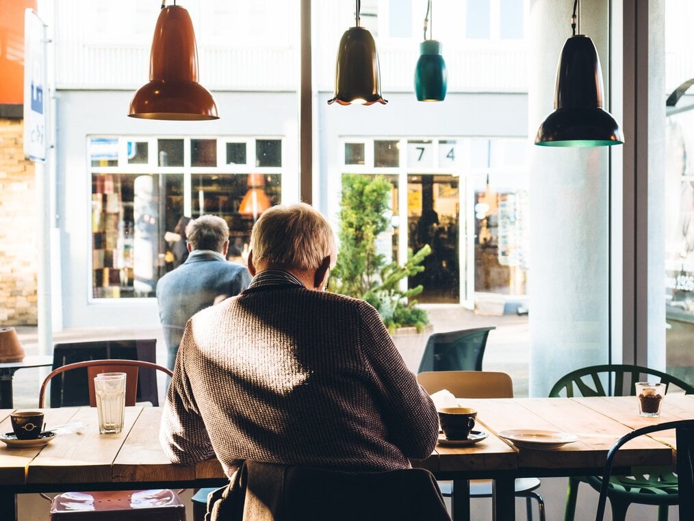 Image curtesy of Jeff Sheldon, Unsplash An older adult sitting at a cafe staring out the window