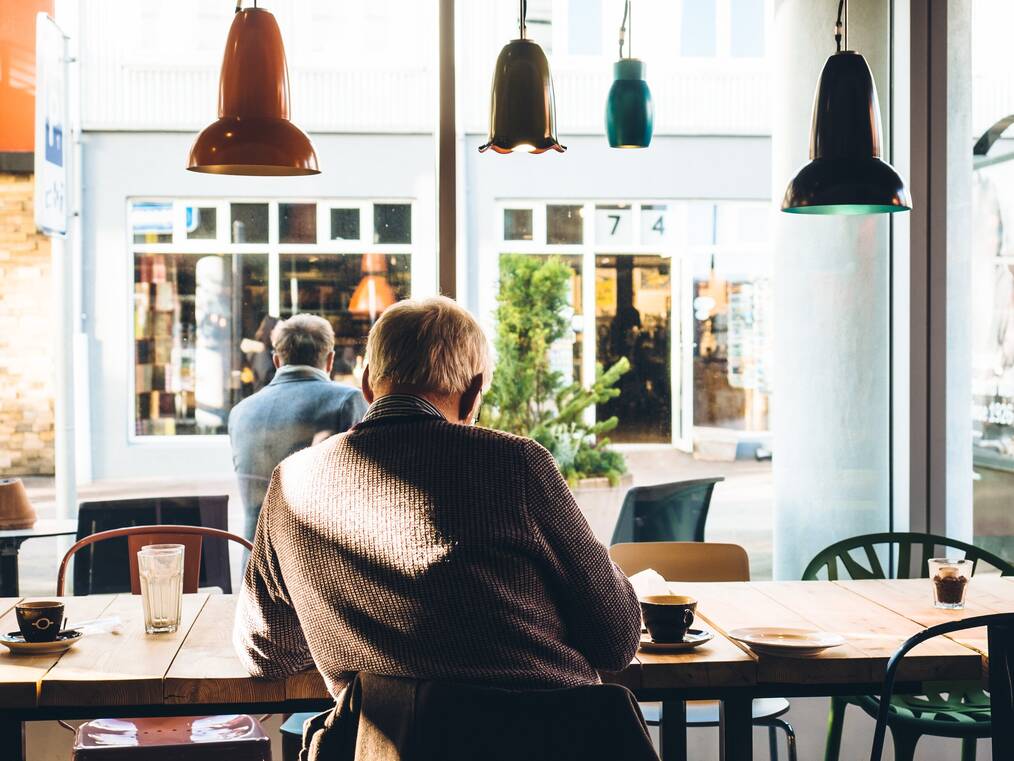 An older adult sitting at a cafe staring out the window
