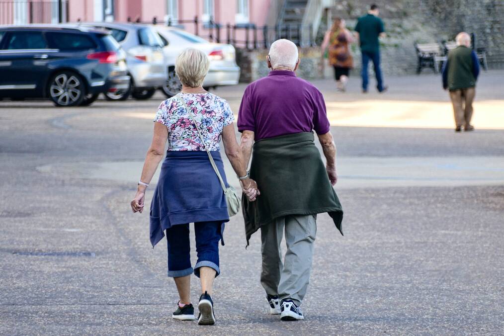 Two older adults holding hands walking down a street