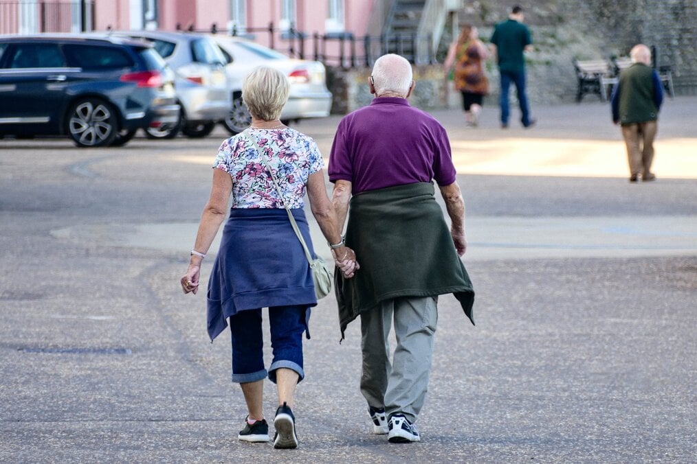 Image curtesy of Mark Timberlake, Unsplash Two older adults holding hands walking down a street