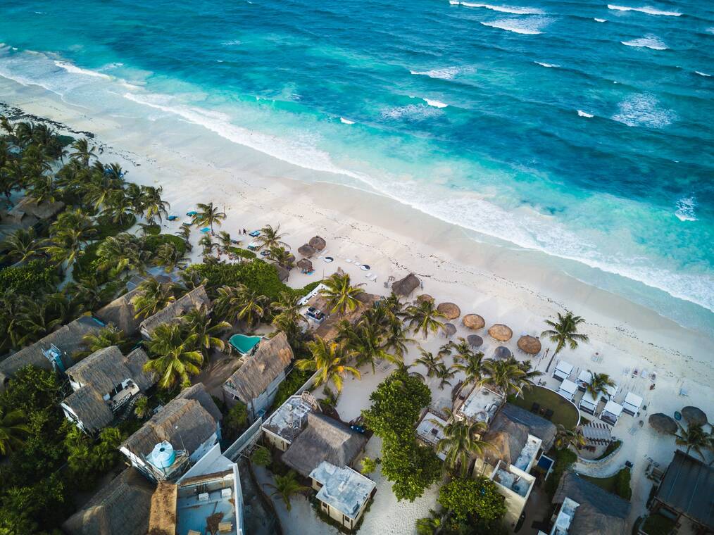 An aerial view of a beach in Mexico with houses, palm trees, and bright blue water