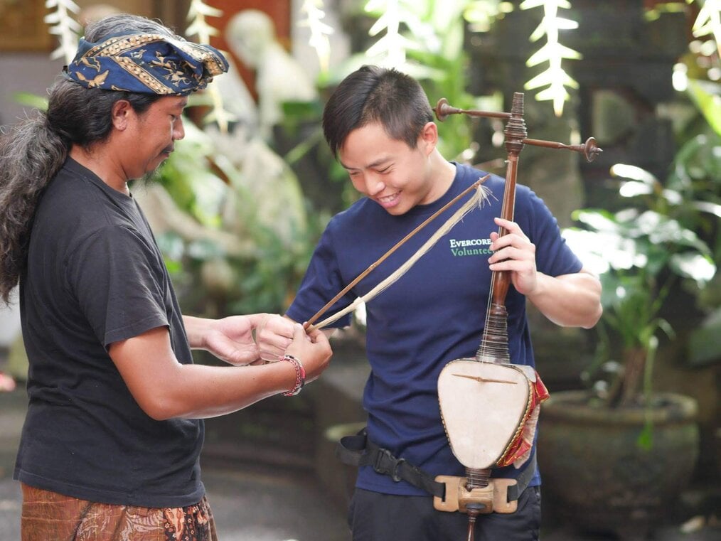 Daniel L., Volunteer Programs Bali Bali A man shows another man a bow used for a traditional instrument.