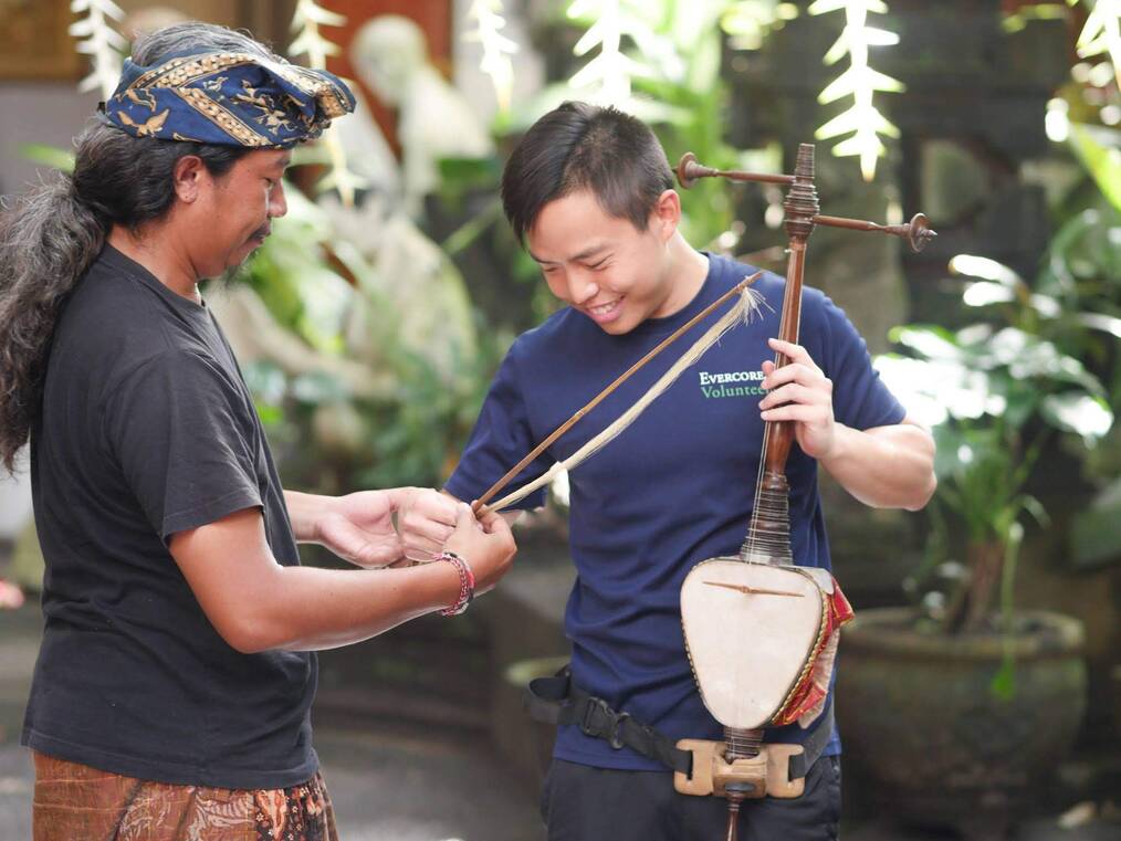 A man shows another man a bow used for a traditional instrument.