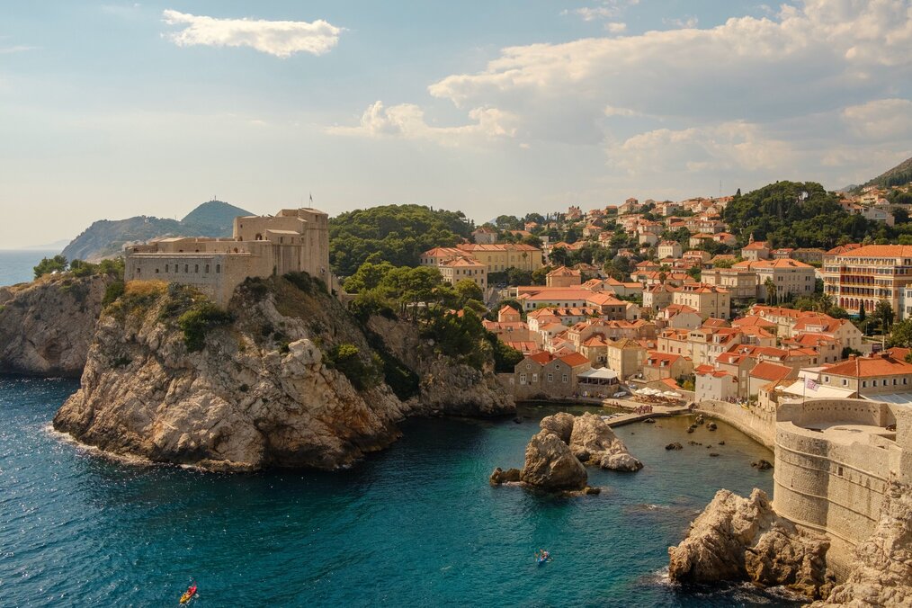 Photo by Morgan on Unsplash A bay of blue water below rocky cliffs with buildings in Dubrovnik, Croatia.